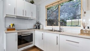 Eine moderne Küche mit weißen Schränken, einem eingebauten Backofen, einem großen Fenster mit Blick ins Grüne und einer Holzarbeitsplatte.