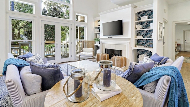 A spacious living room with a fireplace, large windows, and a television. - Gorgeous 7 Bed 6 & 1-2 Bath Home with Private Heated Pool! (Hilton Head Island)
