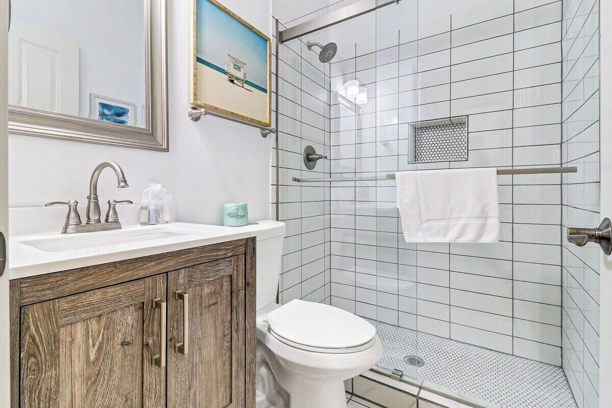 A bathroom with a white sink, wooden cabinet, white toilet, and a glass shower enclosure.