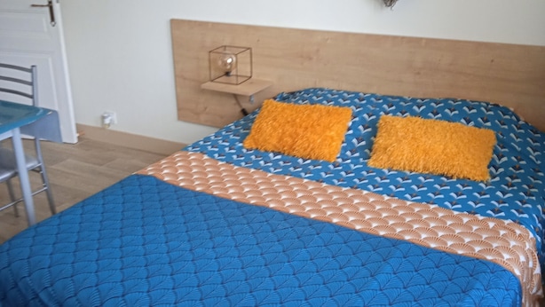 A bedroom with a bed, two pillows, a heart-shaped wall decoration, a small table, and a chair. - Lovely studio 10 les capucines, Bagnoles de l'Orne town center (Bagnoles de l'Orne Normandie)