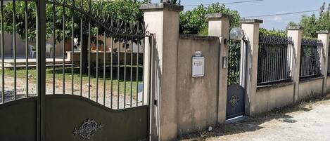 Propiedad amurallada con portón metálico, pared de concreto y un pequeño cuadro eléctrico.