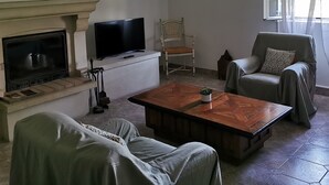 A living room with a fireplace, a television, a coffee table, two sofas, a chair, and a large window with curtains. - At the gateway to the Luberon Regional Nature Park Classified tourist accommodation ★★★ (Cheval-Blanc)