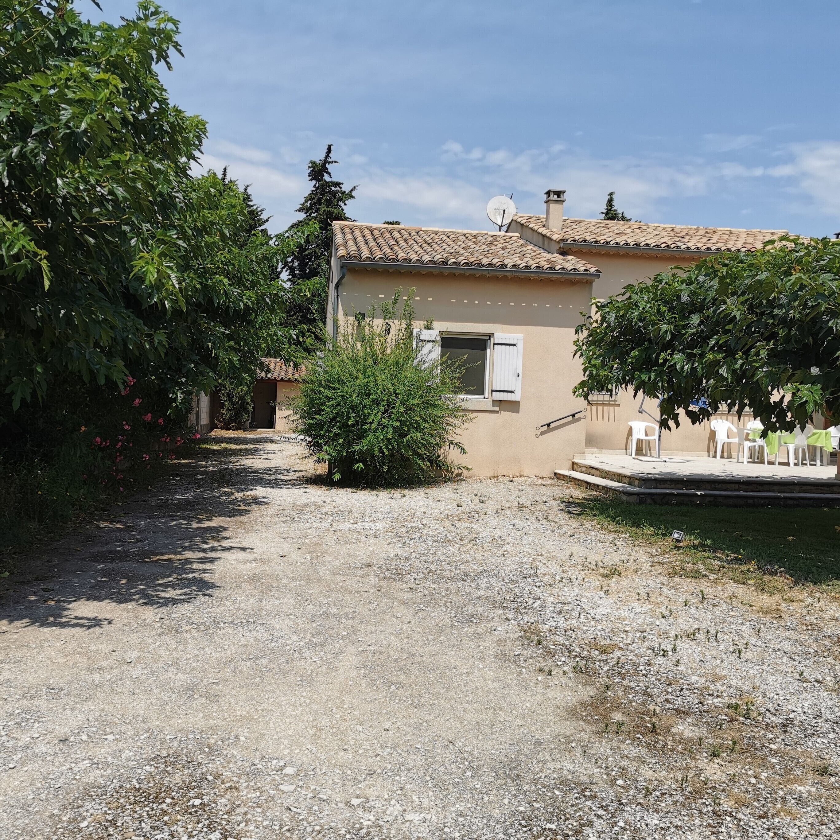 A rustic building with a tiled roof, a gravel driveway, and a small garden area with a bench.