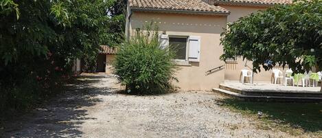A rustic building with a tiled roof, a gravel driveway, and a small garden area with a bench.