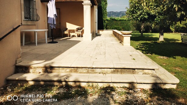 A courtyard with a stone bench, a table, and chairs. There is a building with a tiled roof and a window with a metal grill. - At the gateway to the Luberon Regional Nature Park Classified tourist accommodation ★★★ (Cheval-Blanc)