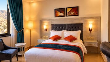 A hotel room with a bed, bedside tables, a lamp, a chair, and artwork on the wall.