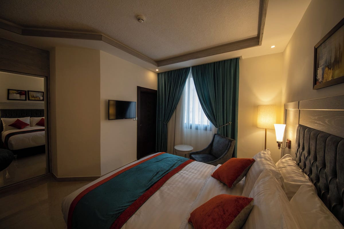 A hotel room with a large bed, a chair, a TV, and a window with curtains.