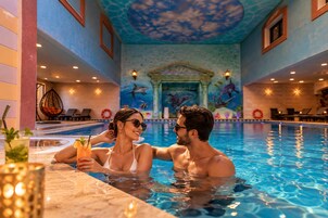 Piscina interior con un mural de delfines, sillas de descanso y zona de bar.
