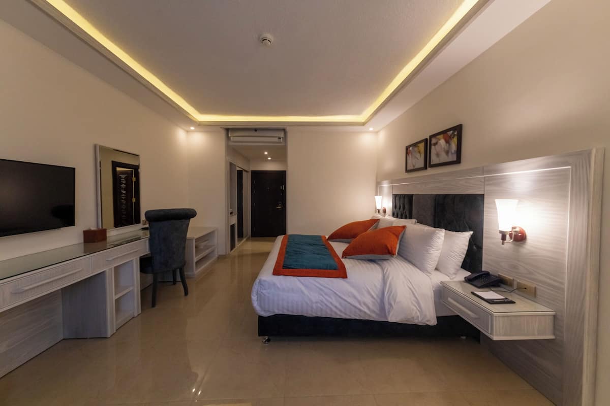 A modern hotel room with a bed, bedside table, TV, desk, and chair.