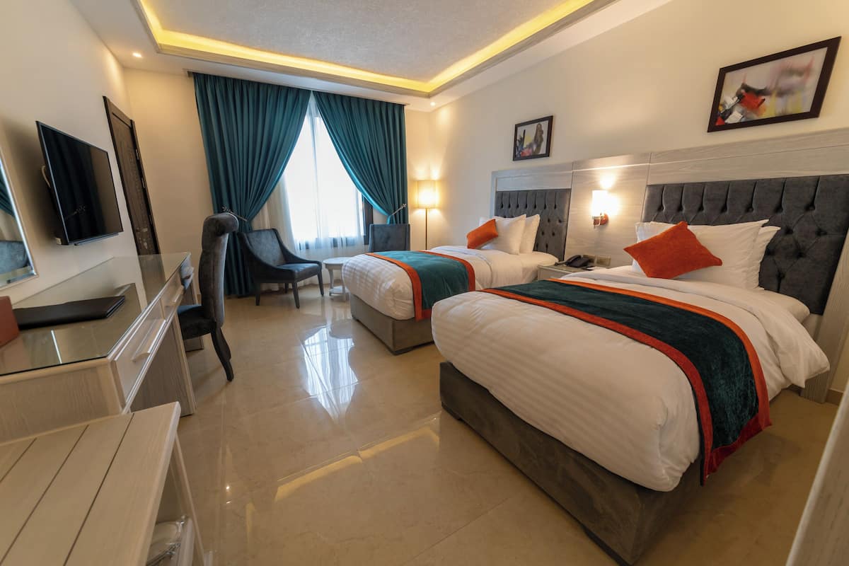 A hotel room with two beds, a desk, a chair, a TV, and a window with curtains.