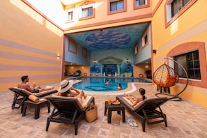 A pool area with lounge chairs, a hanging chair, and a decorative ceiling. - Petra Canyon Hotel (Wadi Musa)
