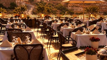 Un espacio de comedor al aire libre con mesas dispuestas para los huéspedes, con vistas a una colina pintoresca al atardecer.