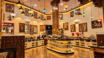 A hotel lobby with a central buffet area, decorative lighting, and artwork on the walls.