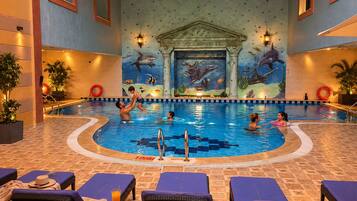 An indoor swimming pool with a mural of marine life on the walls, lounge chairs, and a tiled floor.