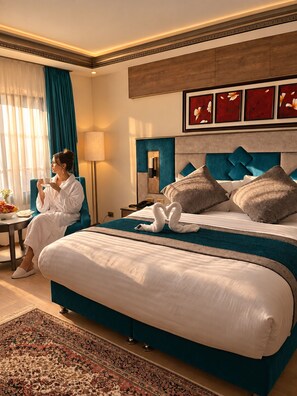Quarto de hotel com uma cama grande, área de estar com mesa e cadeiras, e vista para o exterior.
