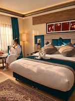 Habitación de hotel con una cama grande, zona de estar con mesa y sillas, y vista al exterior.