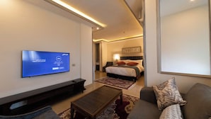 A modern living room with a flat-screen TV, a sofa, a coffee table, and a bedroom with a bed and nightstand. - Petra Canyon Hotel (Wadi Musa)