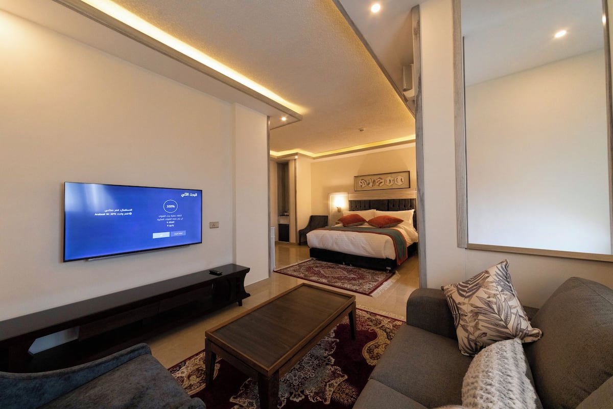 A modern living room with a flat-screen TV, a sofa, a coffee table, and a bedroom with a bed and nightstand.