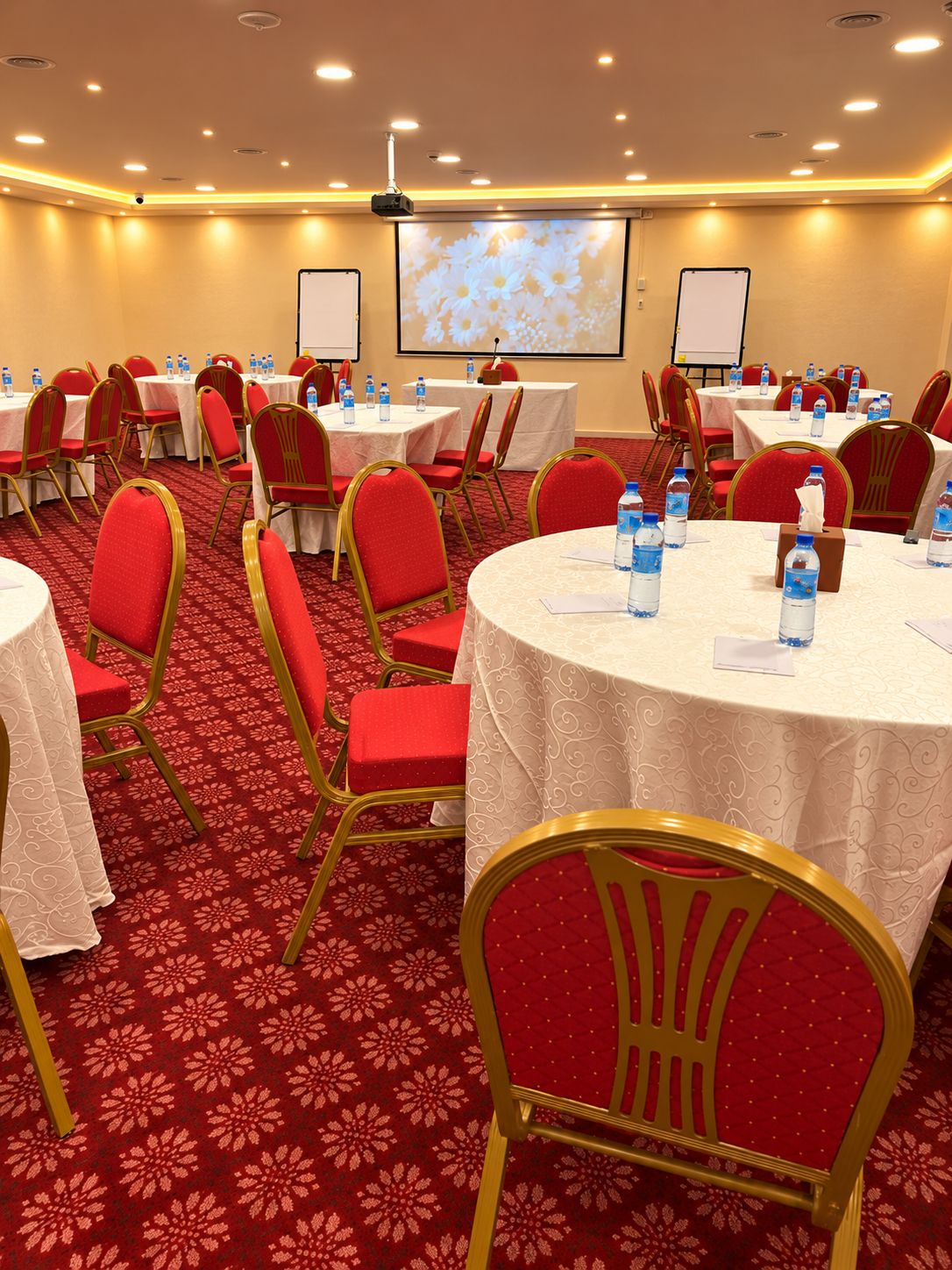 A conference room with round tables, red chairs, and a projector screen.