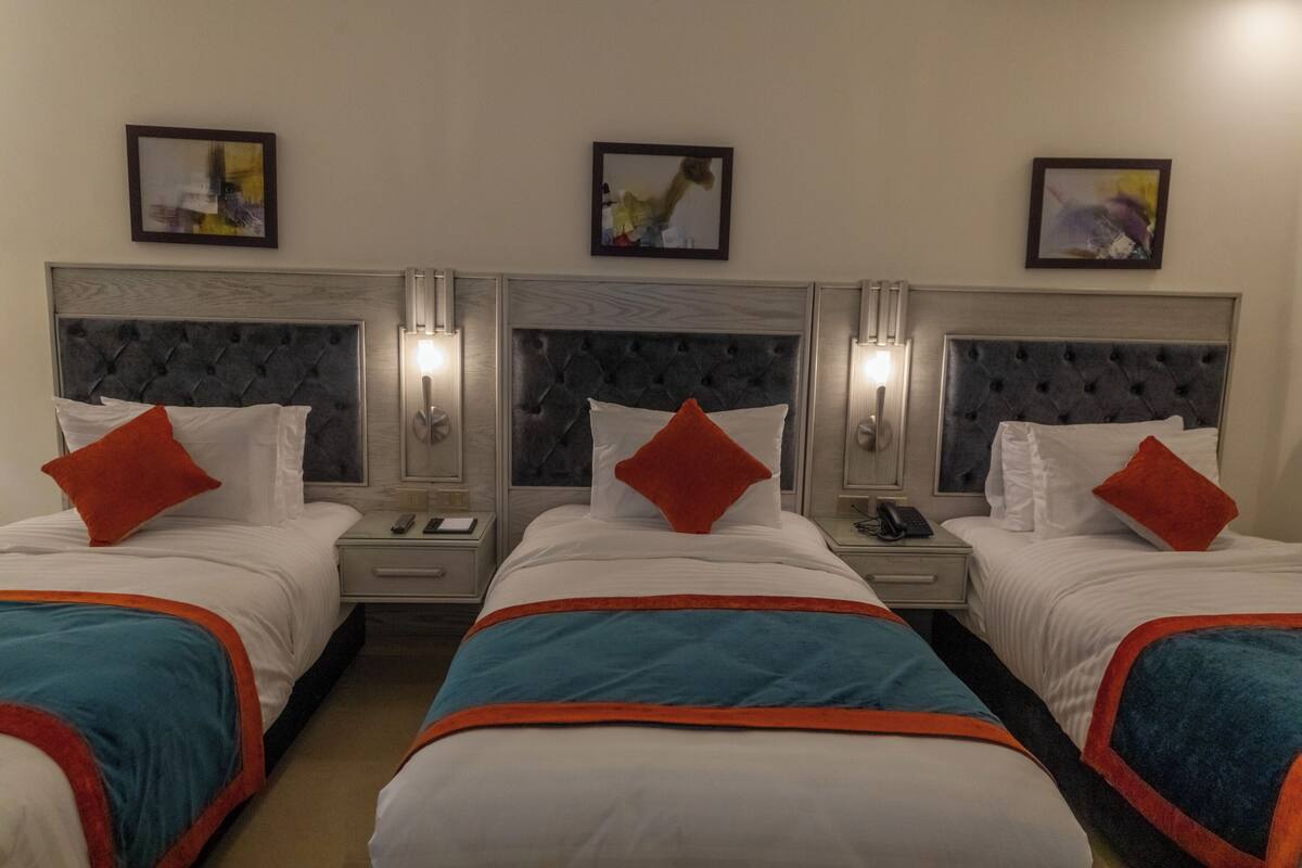 A hotel room with three beds, each with a headboard, bedside tables, and lamps.
