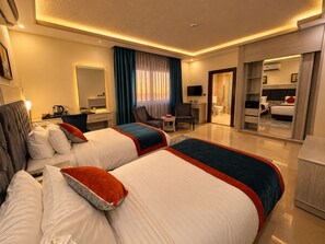 Habitación de hotel con dos camas, un escritorio, una silla, un televisor y un baño visible a través de una puerta abierta.