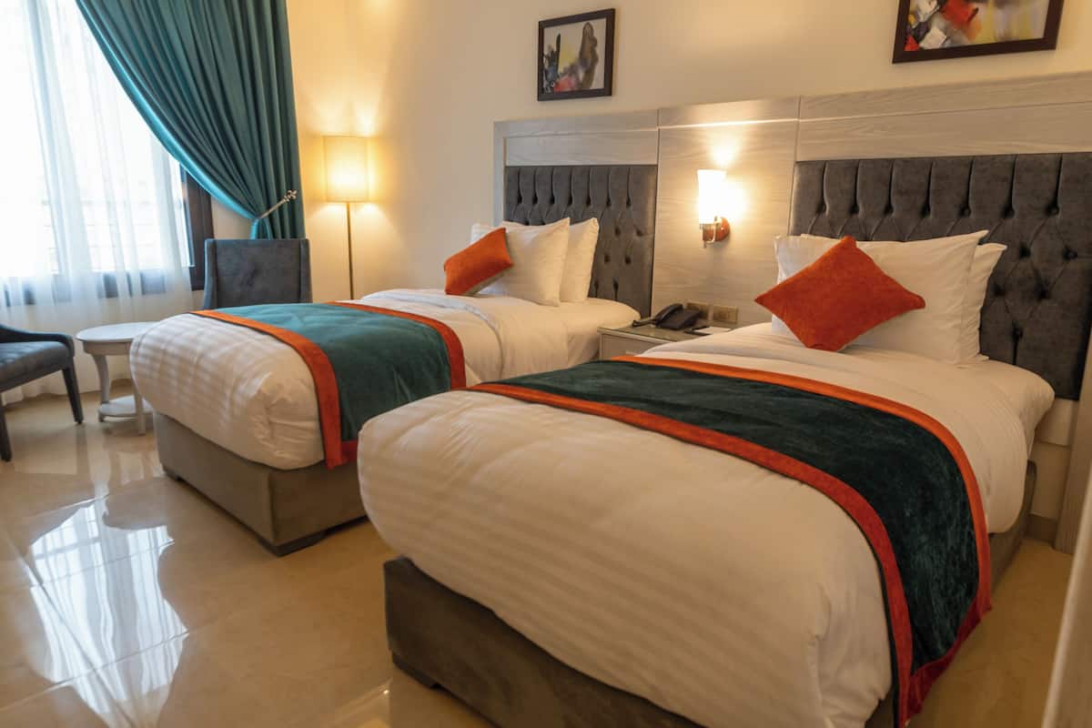 A hotel room with two beds, a nightstand, a chair, and a lamp.