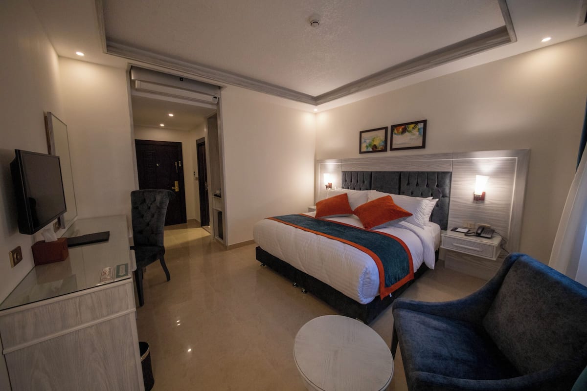 A modern hotel room with a large bed, bedside tables, a TV, and a seating area.