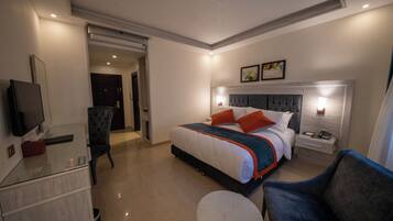 A modern hotel room with a large bed, bedside tables, a TV, and a seating area.