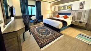 A hotel room with a large bed, a desk, a chair, a small table, and a large rug. - Petra Canyon Hotel (Wadi Musa)