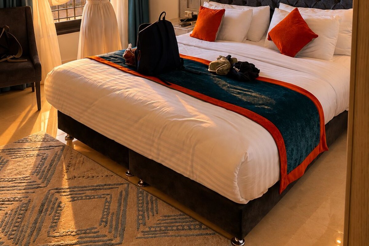 Habitación de hotel con una cama grande, vista al atardecer y una persona de pie junto a la ventana.