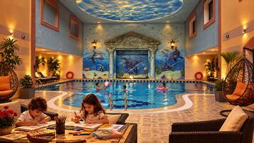 An indoor swimming pool with a mural of marine life on the walls, surrounded by lounge areas and seating.