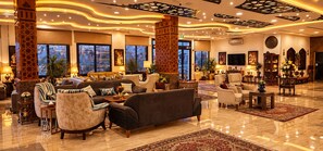 A spacious lobby with a large sofa, armchairs, and a coffee table. There are decorative pillars, a television, and a fireplace. - Petra Canyon Hotel (Wadi Musa)