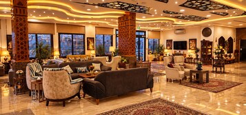 Un vestíbulo espacioso con un sofá grande, sillones y una mesa de centro. Se observan pilares decorativos, un televisor y una chimenea.