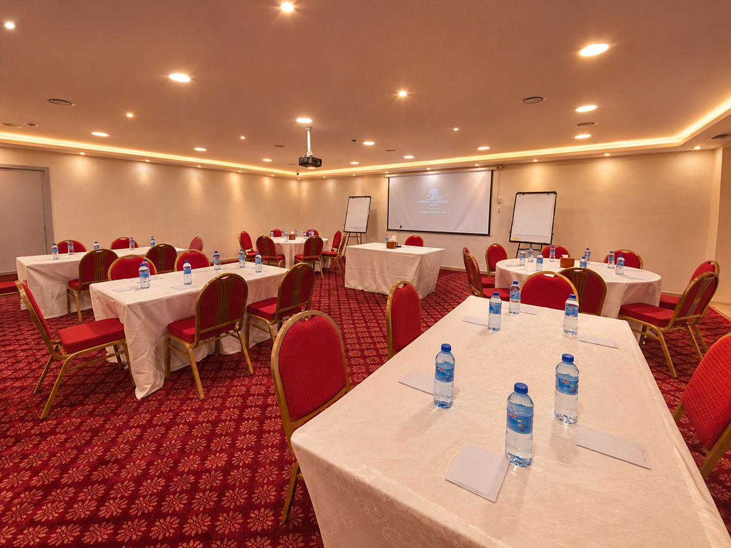 A conference room with tables, chairs, and a projector screen.