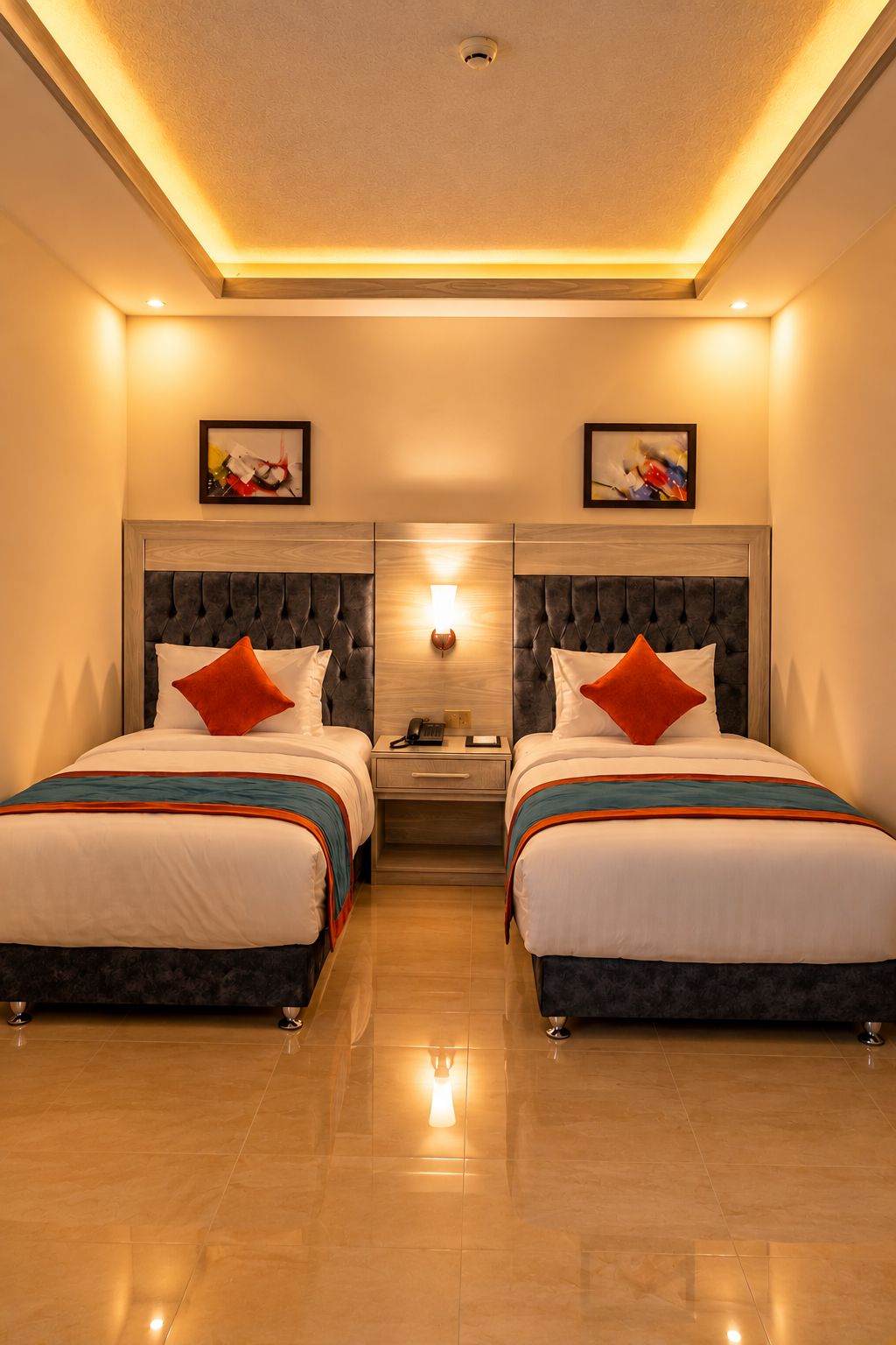 A hotel room with two beds, a nightstand, a wall-mounted lamp, and artwork on the walls.