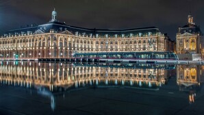 A large, illuminated building with a reflective water surface in front, likely a historic or significant public building.