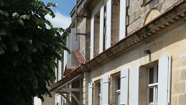 A historic building with a stone facade, multiple windows with shutters, and a small courtyard.