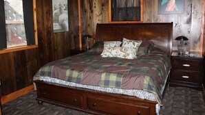 Quarto com painéis de madeira, uma cama grande, duas mesas de cabeceira e uma janela.