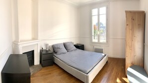 Een slaapkamer met een bed, nachtkastje, dressoir, raam en radiator.