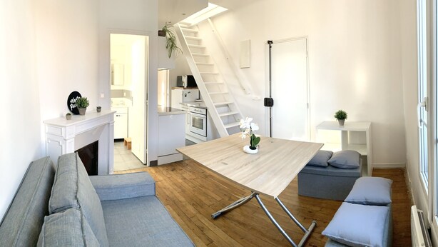 Een moderne woonkamer met een houten tafel, een grijze bank en een trap naar een verdieping erboven.