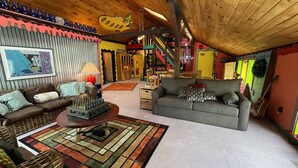 Een gezellige woonkamer met een houten plafond, een schaakbord als middelpunt en een kleurrijk vloerkleed.