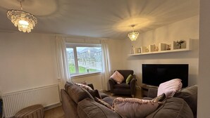 A living room with a brown sofa, a television, and a chandelier. - Carleys House (Macduff)