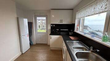 A compact kitchen with a built-in washing machine, a large window with a view of the sea, and a door leading outside.