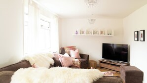 A living room with a sofa, ottoman, television, and decorative items. - Carleys House (Macduff)