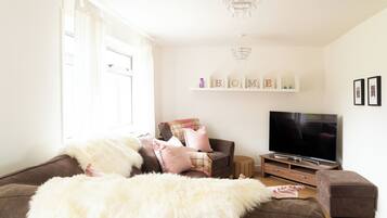 A living room with a sofa, ottoman, television, and decorative items.