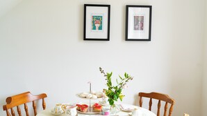 A dining table with a white tablecloth, two framed pictures on the wall, and a vase with flowers. - Carleys House (Macduff)