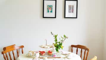 A dining table with a white tablecloth, two framed pictures on the wall, and a vase with flowers.