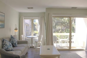 A living room with a sofa, chairs, a table, and a balcony with a view.