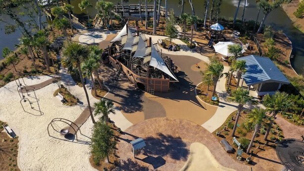 Un parque con zona arenosa, fuente de agua y pabellón con sombra.