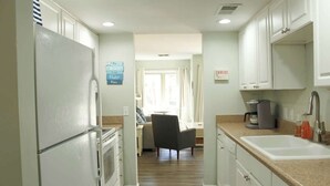 Una cocina con armarios blancos, un refrigerador, un lavamanos y una cafetera.